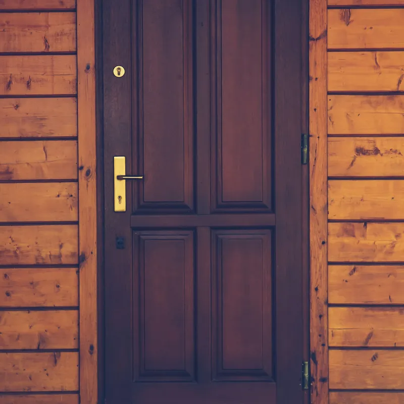 Puerta principal de madera oscura con su chapa en una fachada revestida en madera