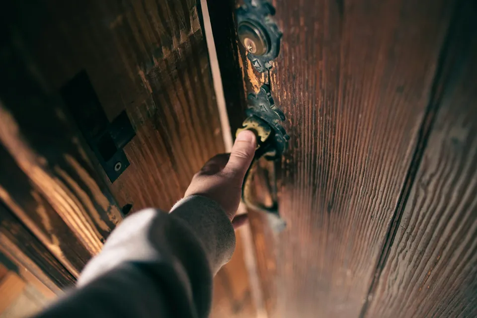 Mano en la manilla de una puerta de madera antigua con llaves en la chapa