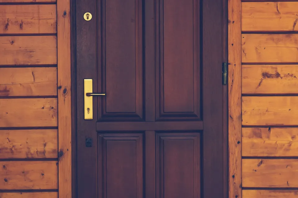Puerta principal de madera oscura con su chapa en una fachada revestida en madera